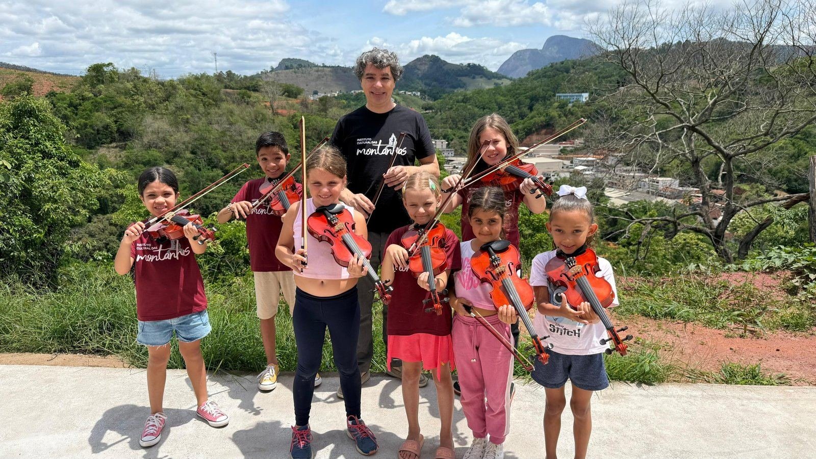 Crianças com violinos ao ar livre, com as montanhas de Afonso Cláudio ao fundo
