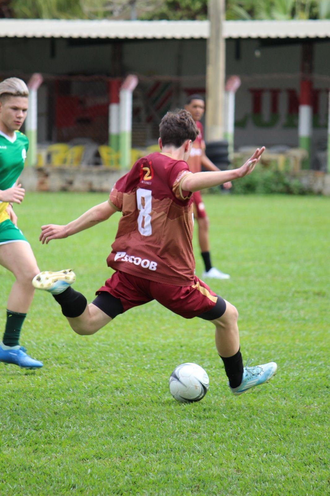 Jovem chutando a bola em jogo de futebol de campo